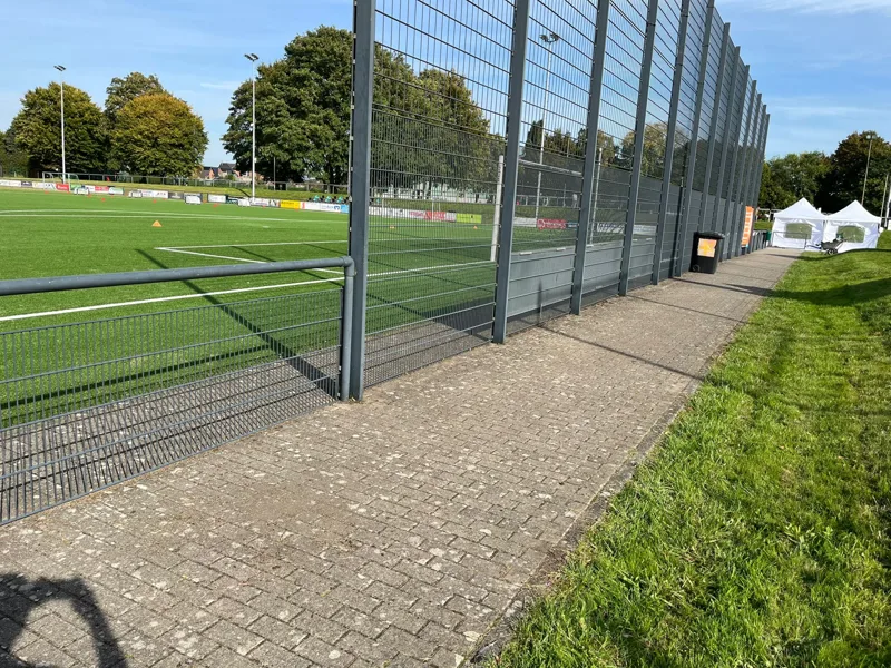 Gepflasterter Weg und Grünstreifen entlang eines Sportplatzes