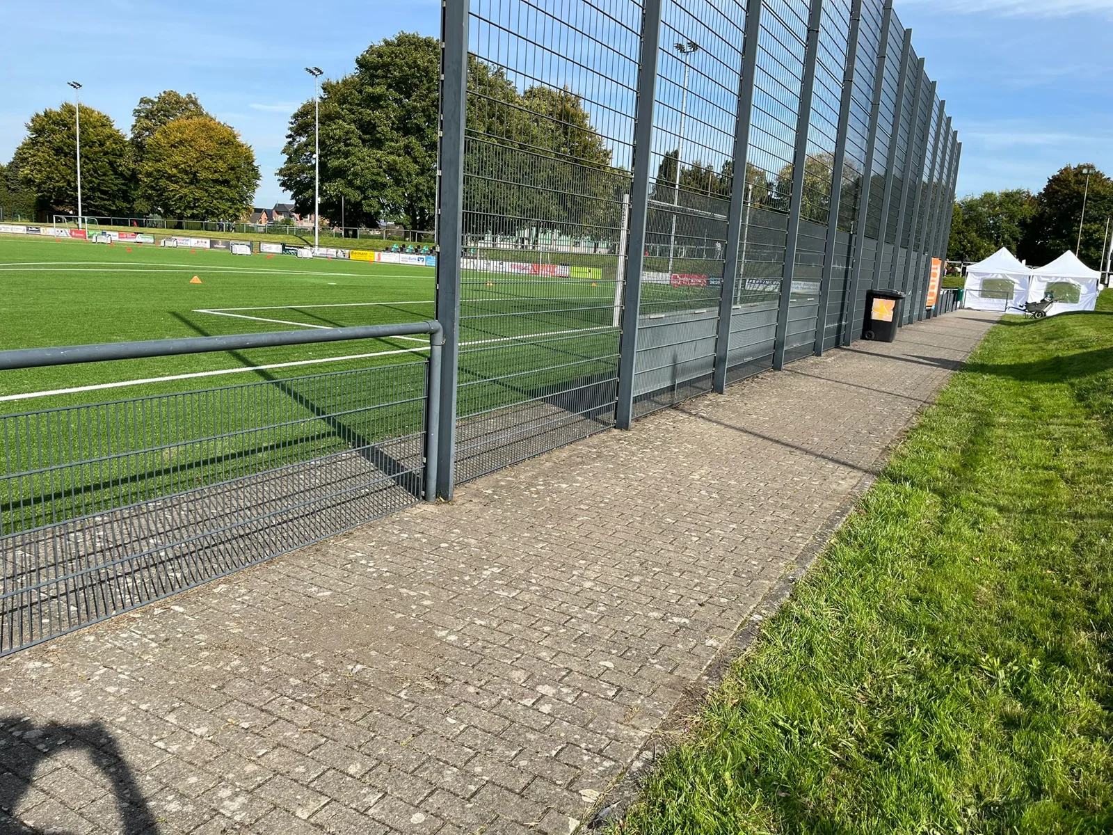 Gepflasterter Weg mit gepflegter Grünfläche an einer Sportanlage