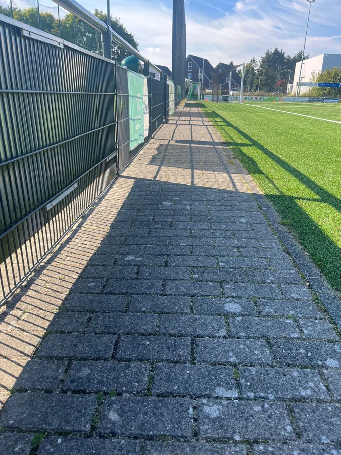 Langer gepflasterter Weg mit Zaunschatten